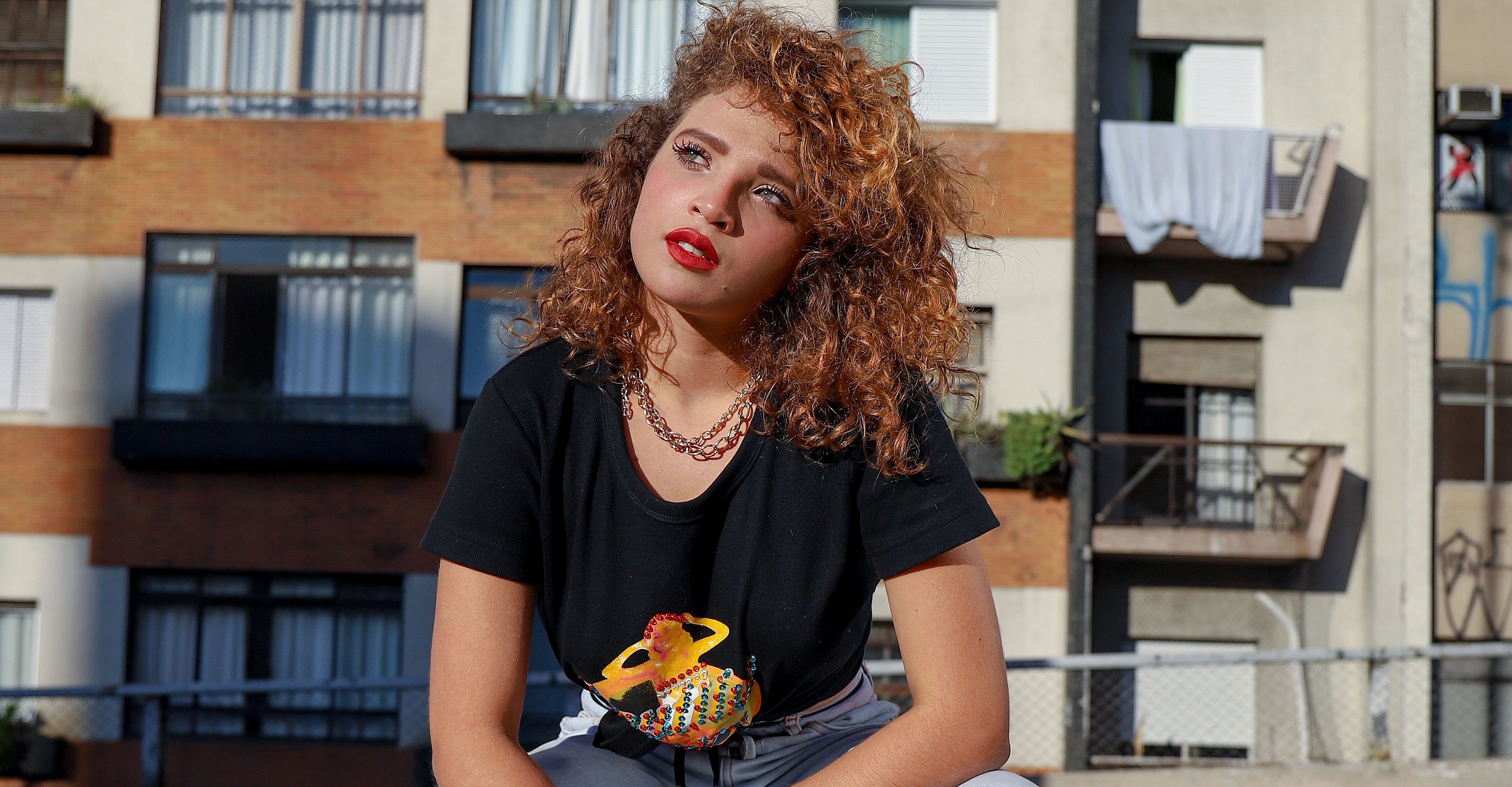 A woman with curly hair and red lipstick in a black t-shirt and jeans.