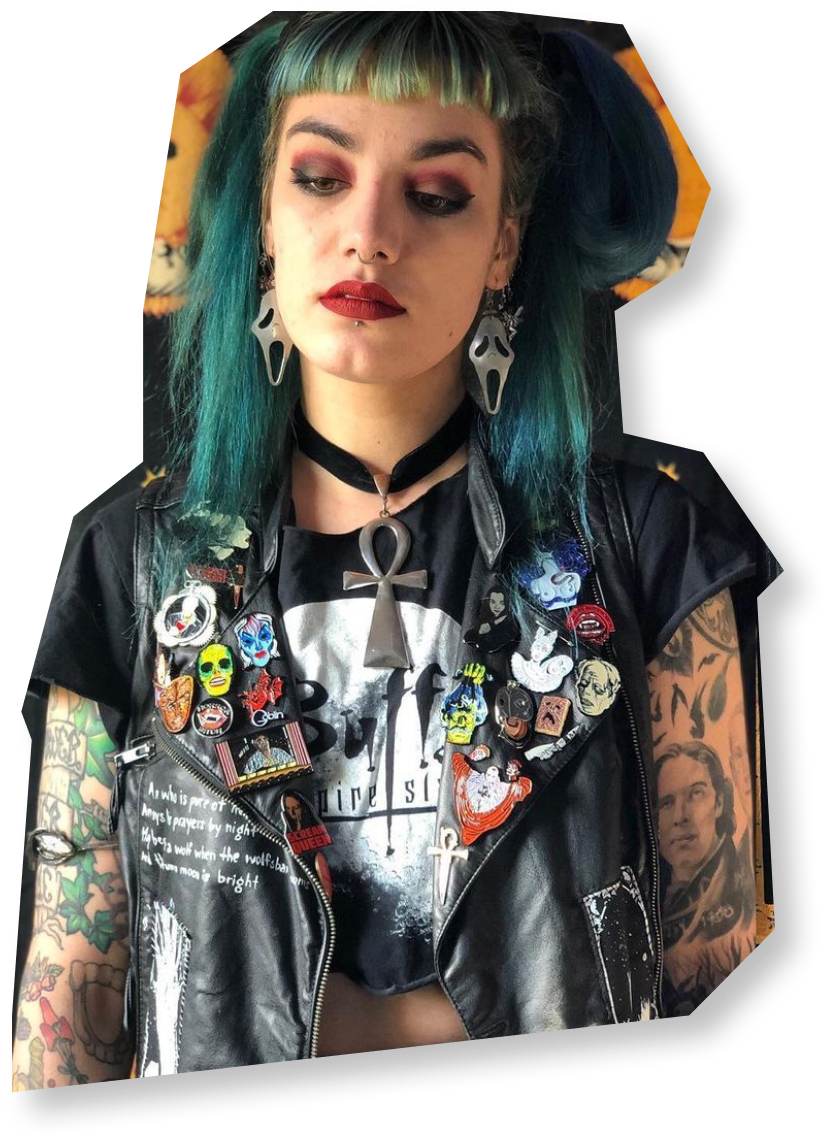 A woman with long blue hair, a cropped jacket with horror-themed pins, and earrings with Ghostface from Scream.