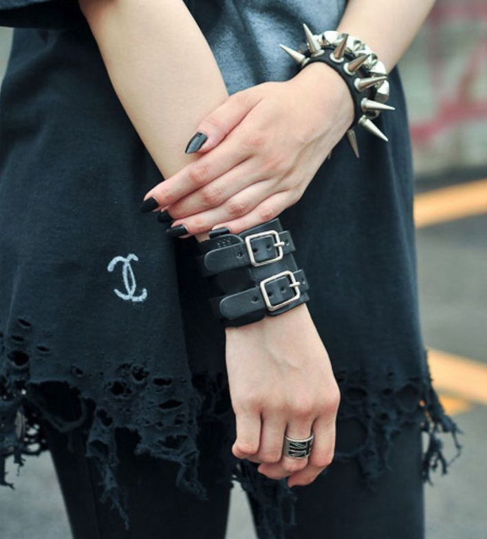 A photograph of a person's hands with belt-style bracelets on one hand and a studded, spiked bracelet on the other hand.