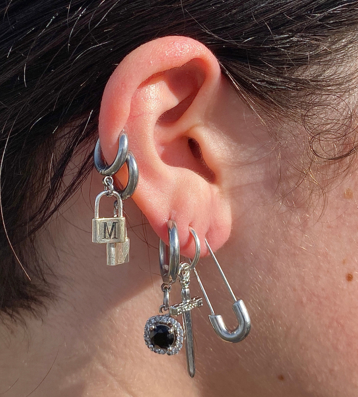 A photo of someone's ear with eccentric earrings such as safety pins, locks, heavy metal rings, and a sword.